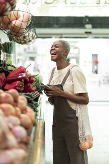 Lachende Frau beim Lebensmitteleinkauf in einer Markthalle - AFVF05890