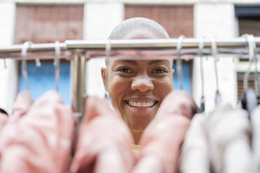 Portrait of happy woman behind clothes rail - AFVF05917