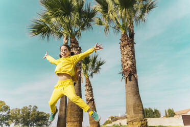 Portrait of little girl jumping in the air in front of palms - ERRF02937