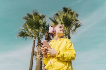 Little girl wearing yellow jacket listening music with headphones and smartphone - ERRF02944