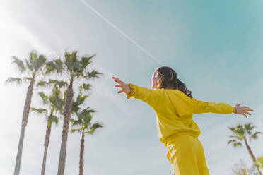 Back view of little girl with arms outstretched listening music with headphones outdoors - ERRF02950