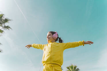 Happy little girl wearing with arms outstretched listening music with headphones outdoors - ERRF02951