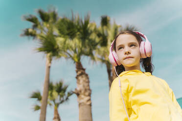Portrait of serious little girl listening music with headphones outdoors - ERRF02952