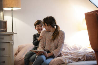 Mutter und kleiner Sohn sitzen zusammen auf dem Bett mit digitalem Tablet und haben Spaß - KNSF07938