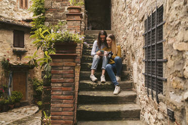 Zwei junge Frauen sitzen auf einer Treppe und schauen auf ihr Smartphone, Greve in Chianti, Toskana, Italien - JPIF00562