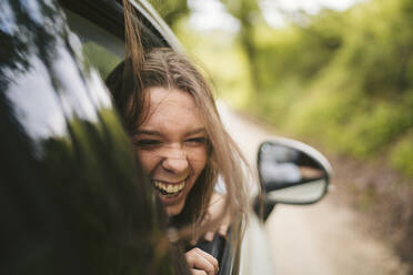 Carefree young woman leaning out of car window - JPIF00577