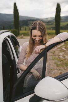 Glückliche junge Frau, die in ländlicher Landschaft in ein Auto steigt, Toskana, Italien - JPIF00586