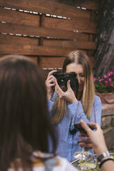 Junge Frau beim Fotografieren eines Freundes mit einem Glas Rotwein im Freien - JPIF00591