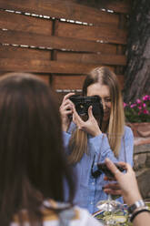 Young woman taking picture of friend having a glass of red wine outdoors - JPIF00591