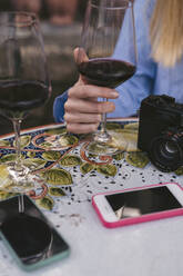 Close-up of woman at table with glass of red wine, camera and cell phones - JPIF00592