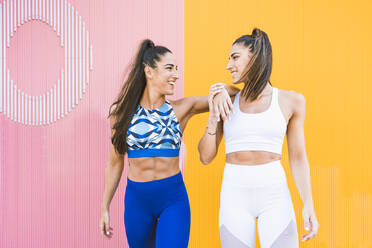 Lächelnde, sportliche Zwillinge posieren vor einer gelb-rosa Wand - DAMF00277