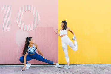 Smiling sportive twins posing in front of a yellow and pink wall - DAMF00282