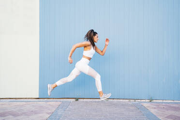 Junge Frau joggt vor blauer und grüner Wand - DAMF00287