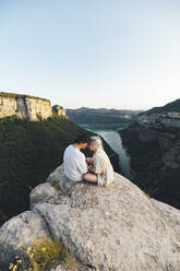 Junges verliebtes Paar auf einem Aussichtspunkt sitzend, Stausee Sau, Katalonien, Spanien - AMAF00011