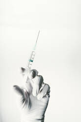 Hand mit Schutzhandschuh, die eine Spritze mit Impfstoff hält - JCMF00489