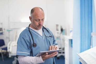 Male doctor using digital tablet in hospital room - CAIF24737
