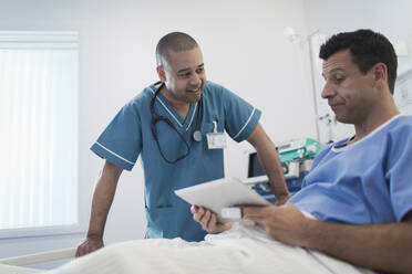 Krankenpfleger im Gespräch mit einem Patienten, der ein digitales Tablet im Krankenhausbett benutzt - CAIF24740
