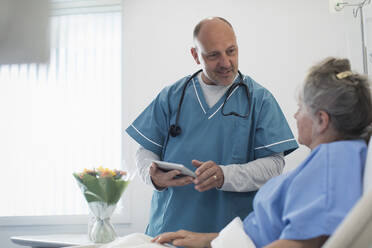 Arzt mit digitalem Tablet bei der Visite, Gespräch mit älterem Patienten im Krankenhauszimmer - CAIF24744