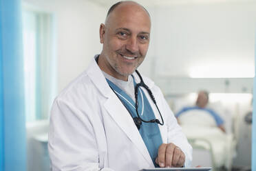 Portrait confident, smiling male doctor using digital tablet in hospital room - CAIF24748