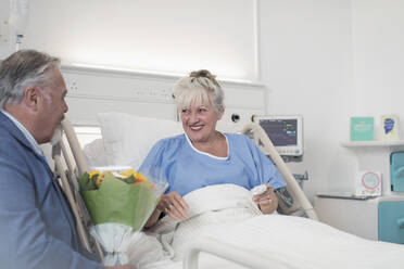 Älterer Mann mit Blumenstrauß besucht Frau im Krankenhaus - CAIF24752