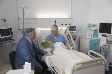 Senior man with flower bouquet visiting wife resting in hospital room - CAIF24765