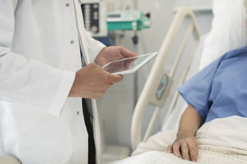 Arzt mit digitalem Tablet bei der Visite, Überprüfung eines Patienten im Krankenhausbett - CAIF24767