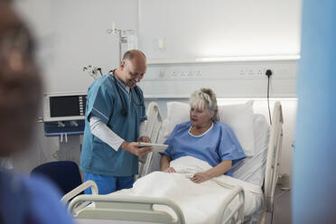 Arzt mit digitalem Tablet bei der Visite, Gespräch mit älterem Patienten im Krankenhauszimmer - CAIF24769