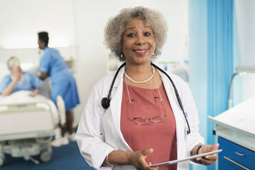 Portrait confident senior female doctor using digital tablet in hospital room - CAIF24771