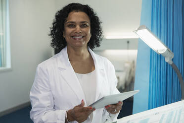 Portrait confident, smiling female doctor using digital tablet in hospital room - CAIF24775