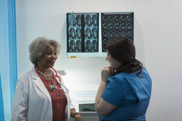 Female doctor and nurse discussing x-rays in in hospital - CAIF24776