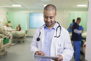 Lächelnder männlicher Arzt mit digitalem Tablet bei der Visite in einer Krankenstation - CAIF24795