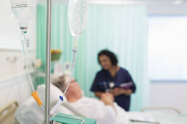 Arzt spricht mit Patientin hinter IV-Tropfen im Krankenhauszimmer - CAIF24798