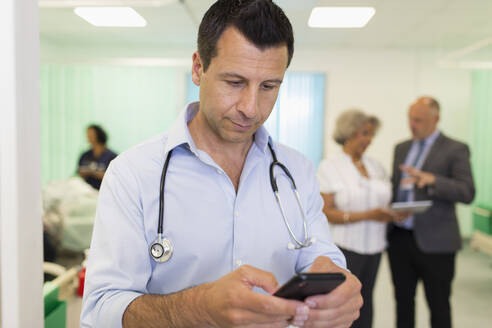 Männlicher Arzt, der ein Smartphone in einer Krankenstation benutzt - CAIF24800