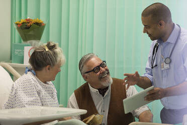 Arzt mit digitalem Tablet bei der Visite, Gespräch mit älterem Ehepaar im Krankenhauszimmer - CAIF24818