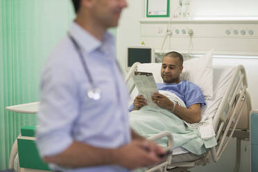 Männlicher Patient liest Zeitung und ruht sich im Krankenhauszimmer aus - CAIF24823