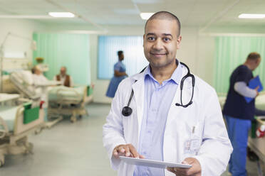 Porträt eines selbstbewussten männlichen Arztes bei der Visite, der ein digitales Tablet in einer Krankenhausabteilung benutzt - CAIF24835