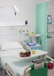 Blumen auf einem Tablett über einem Krankenhausbett in einem leeren Krankenhauszimmer - CAIF24844