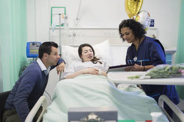 Arzt mit digitalem Tablet bei der Visite, Gespräch mit Paar im Krankenhauszimmer - CAIF24850