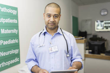 Portrait confident male doctor with digital tablet in hospital corridor - CAIF24863