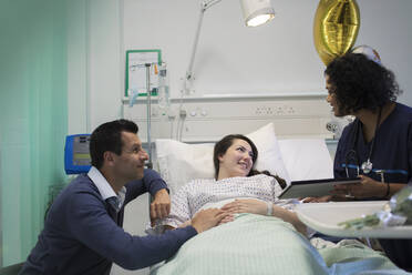 Arzt mit digitalem Tablet bei der Visite, Gespräch mit Paar im Krankenhauszimmer - CAIF24871