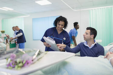 Arzt mit Krankenblatt bei der Visite, Gespräch mit Besucher auf der Krankenstation - CAIF24873