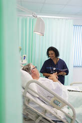 Arzt mit digitalem Tablet bei der Visite, Gespräch mit älterem Patienten im Krankenhauszimmer - CAIF24874