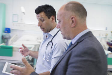 Männliche Ärzte mit digitalem Tablet bei der Visite, Beratung im Krankenhauszimmer - CAIF24883