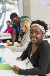 Portrait confident female student with paperwork in classroom - CAIF24891