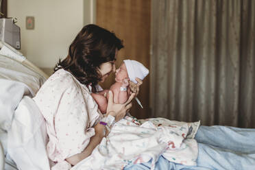 Seitenansicht von Mutter und neugeborenem Sohn, die sich im Krankenhaus die Nasen berühren - CAVF77661