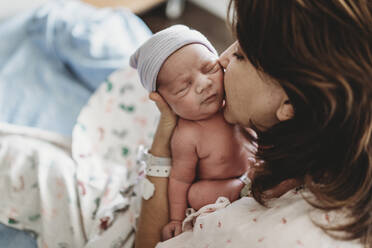 Close up detail of mother kissing newborn son's cheek in hospital - CAVF77662