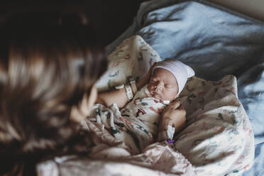 Draufsicht auf eine Mutter, die einen neugeborenen Jungen mit Hut im Krankenhausbett hält - CAVF77666