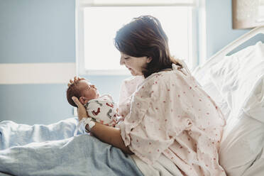 Side view of mother looking lovingly at newborn son in hospital - CAVF77677