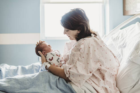 Seitenansicht einer Mutter, die ihren neugeborenen Sohn im Krankenhaus liebevoll betrachtet - CAVF77677