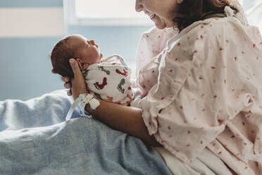 Side view of mother looking and smiling at newborn son in hospital - CAVF77678